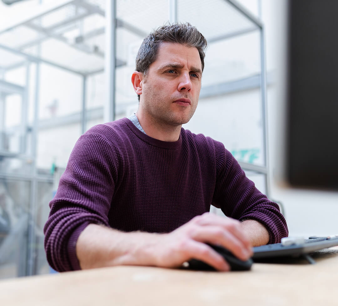 Man sitting at desk in front of a computer with computer mouse in right hand