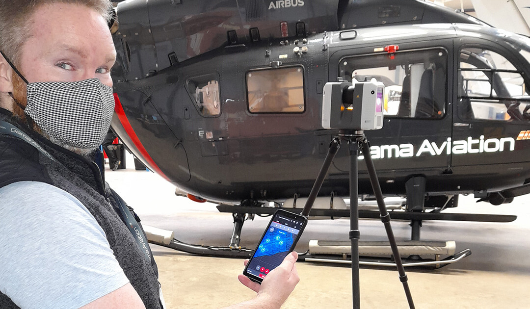 Ross Graham standing with mobile phone next to a black helicopter with the text Gama Aviation on it